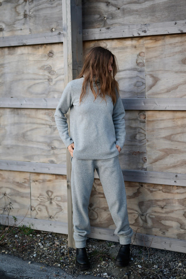 Person wearing a gray tracksuit standing against a wooden wall.