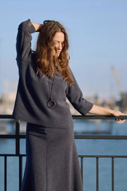 Woman in a navy outfit standing by a waterfront with boats in the background