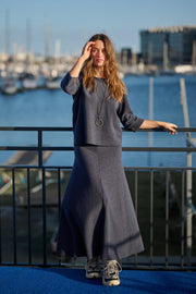 Woman in a navy outfit standing by a waterfront with boats and buildings in the background