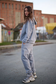 Woman wearing a gray tracksuit standing on a street with buildings in the background