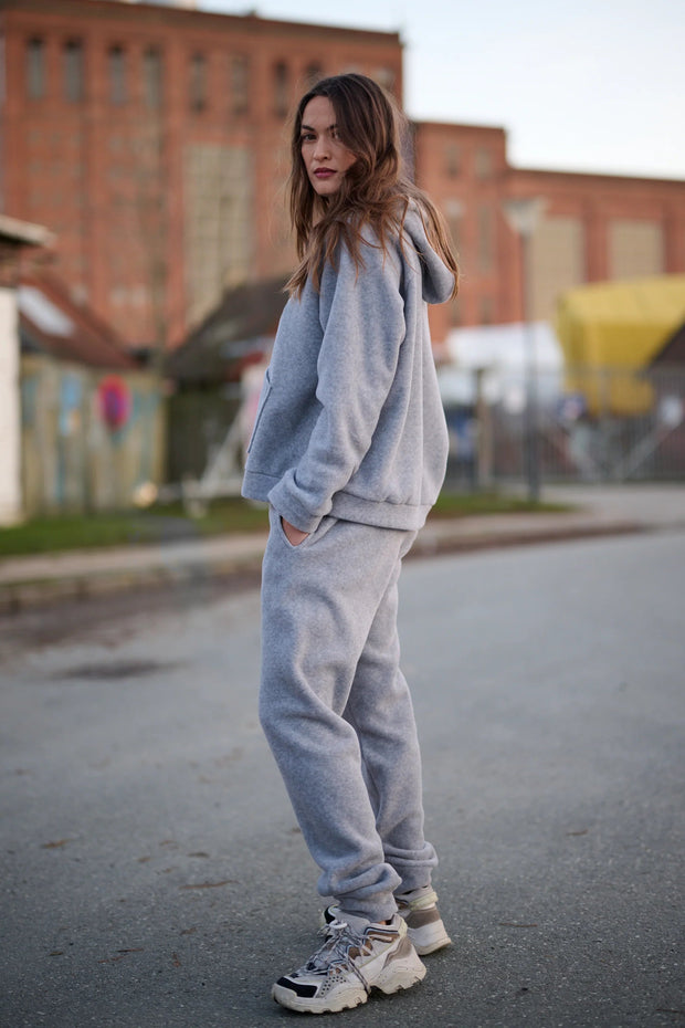 Woman wearing a gray tracksuit standing on a street with buildings in the background