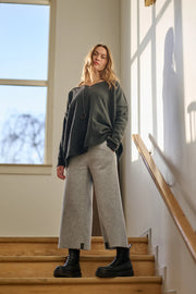 Woman standing on a staircase wearing a dark grey sweater and light gray pants.