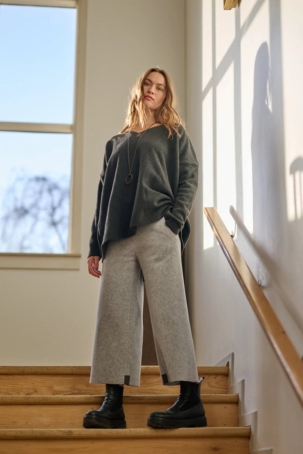 Woman standing on a staircase wearing a dark grey sweater and light gray pants.