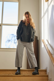Woman standing on a staircase wearing a gray sweater and light gray pants.