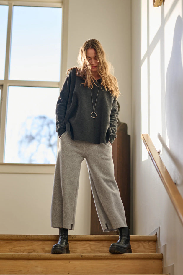 Woman standing on a staircase wearing a gray sweater and light gray pants.