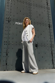Woman in a white top and gray pants standing in front of a large metallic door with 'PORT' written on it.