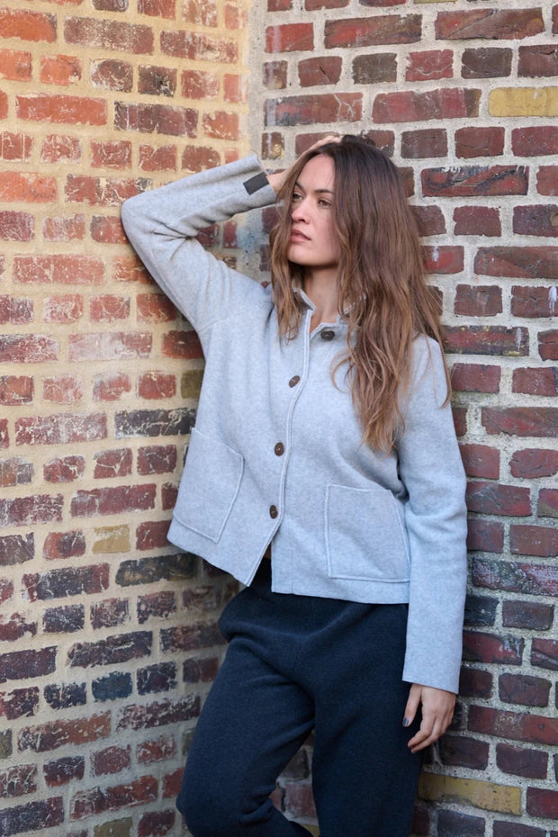 Woman wearing a light gray jacket against a brick wall