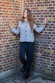 Woman leaning against a brick wall wearing a gray jacket and dark pants.
