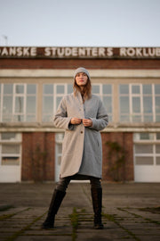 Person wearing a long coat and knee-high boots standing in front of a building with 'Danske Studenters Roklub' sign.