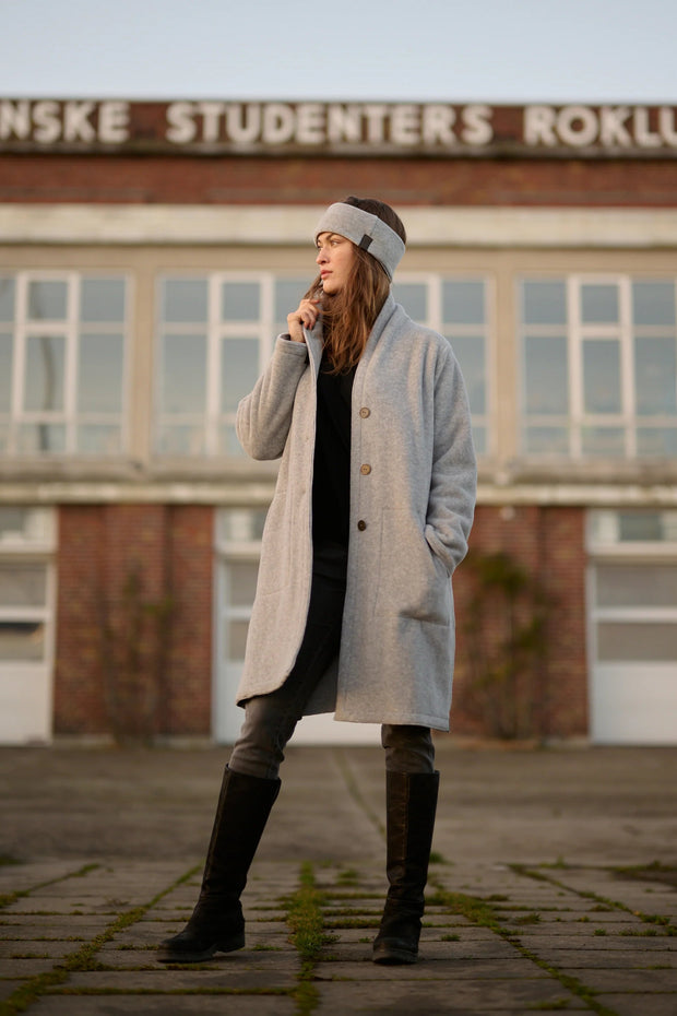 Person wearing a long coat and knee-high boots standing in front of a building with text on it.
