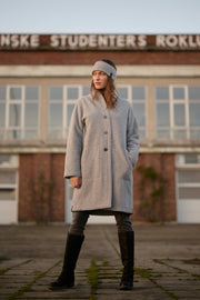 Person wearing a gray coat standing in front of a building with text on it