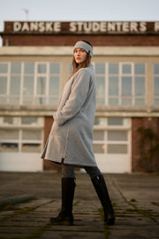 Woman in a long gray coat standing in front of a building with 'Danske Studenters' sign.